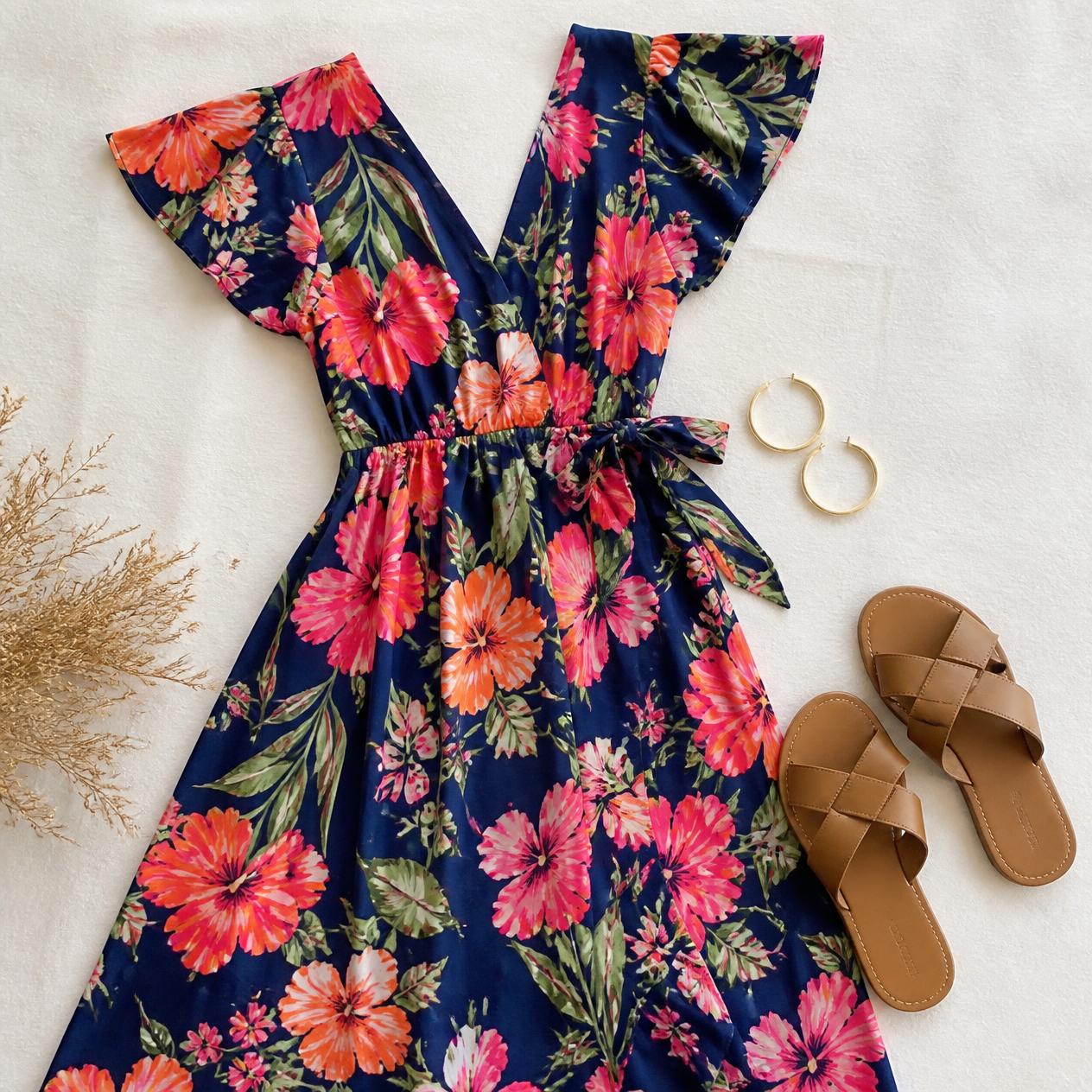 Overhead flatlay photo of a bold floral-print wedding guest dress with gold hoop earrings and tan sandals