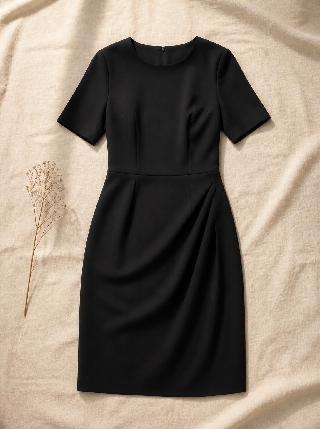 Simple black knee-length dress laid flat with the sleeves smoothed on a cream background