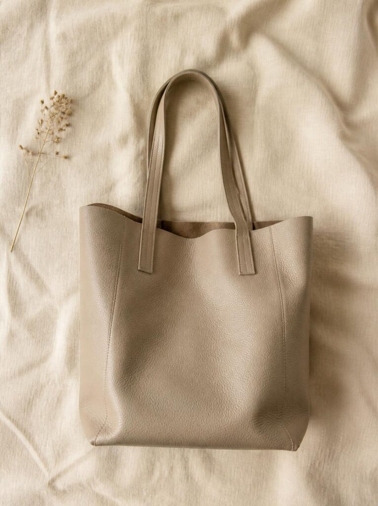 Simple neutral leather tote bag placed upright with the top slightly open on a cream background