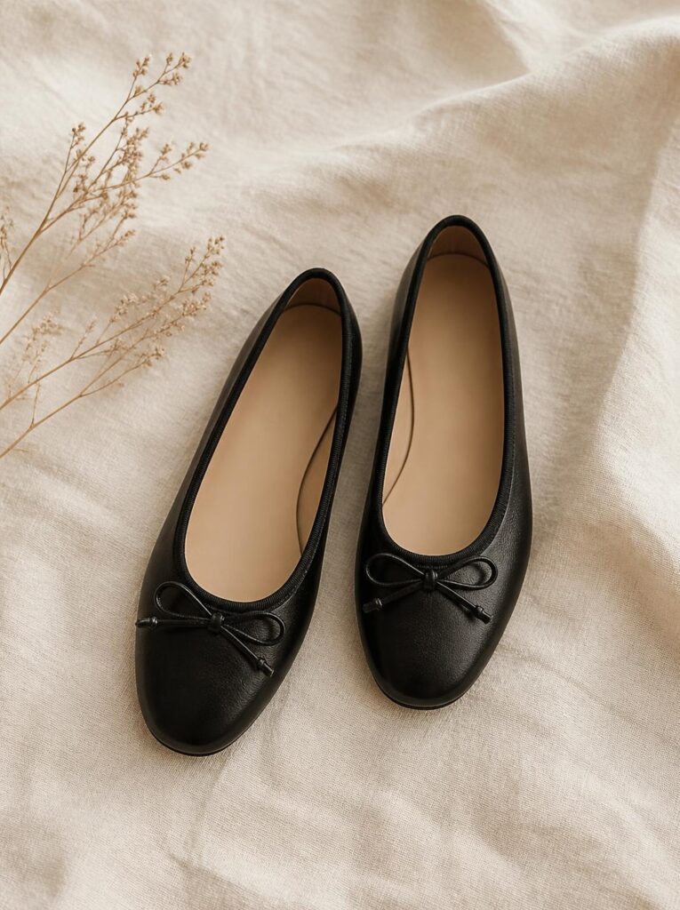 Pair of black leather ballet flats placed side by side at a slight angle on a cream background