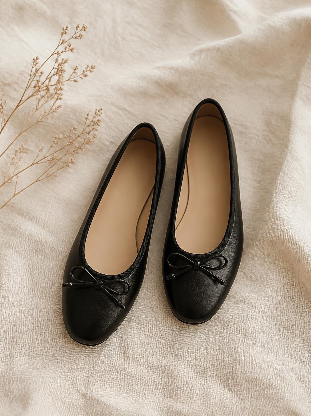 Pair of black leather ballet flats placed side by side at a slight angle on a cream background